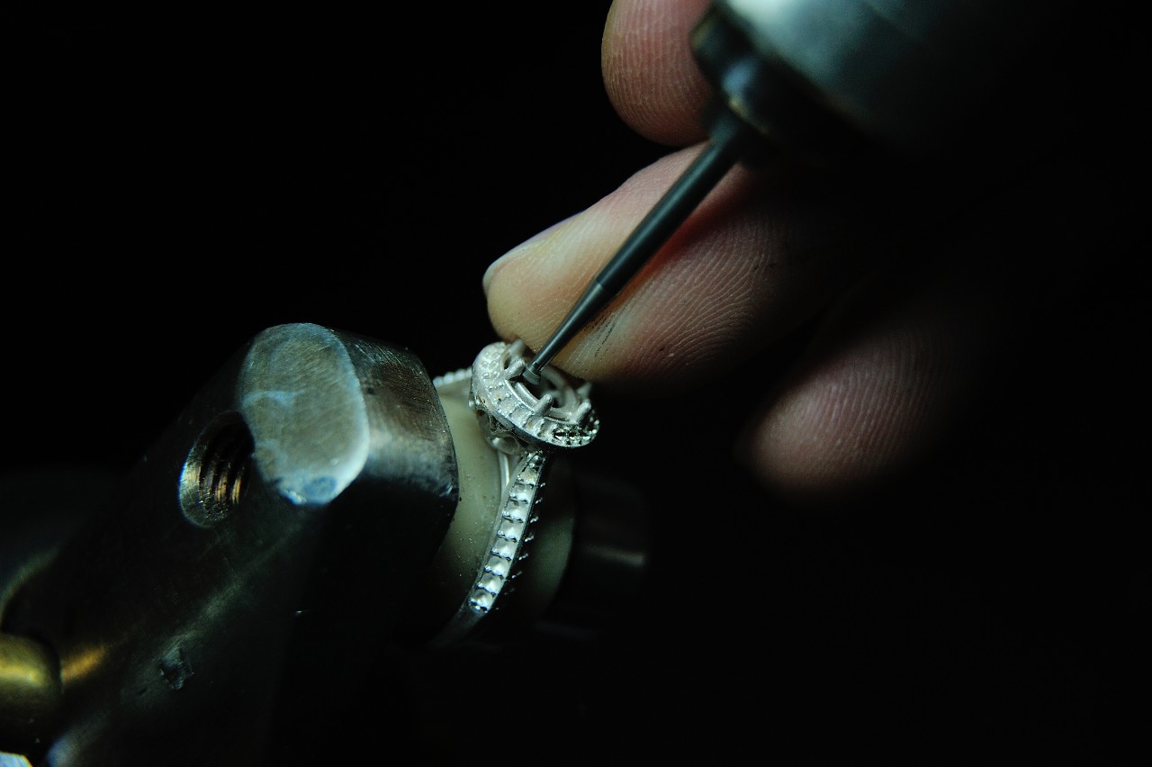 A close-up of a craftsman using a tool to secure a setting in a white gold engagement ring.