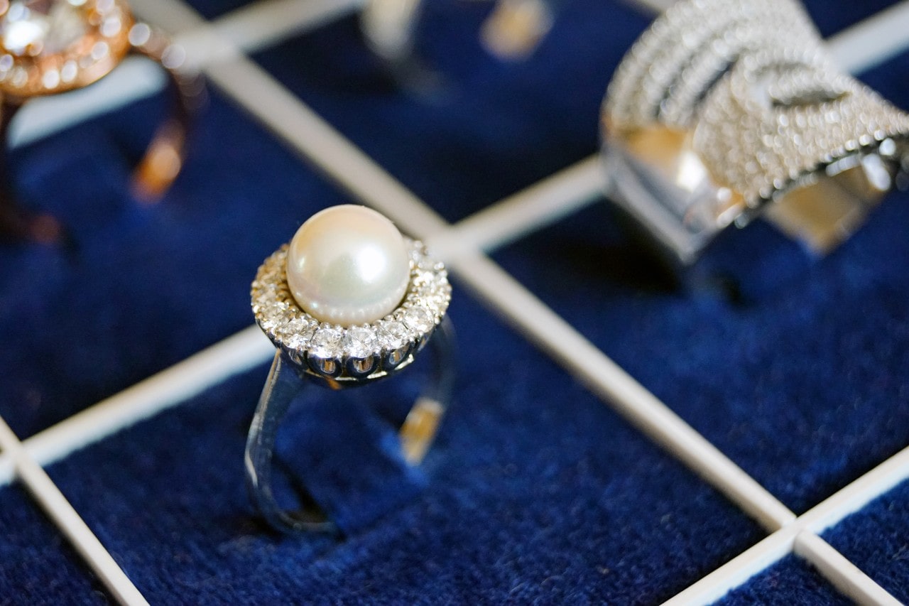 A close-up of a pearl ring with a diamond halo set against a deep blue velvet background.
