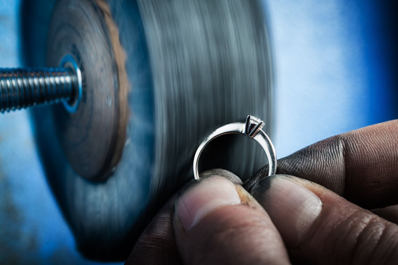 A close up of a jeweler who refines a diamond engagement ring against a rotating polishing wheel