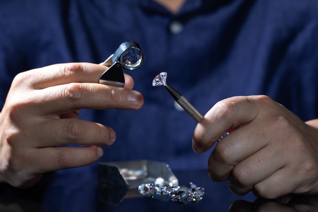 A close up of a jeweler in a deep blue shirt inspecting diamond with magnifying glass