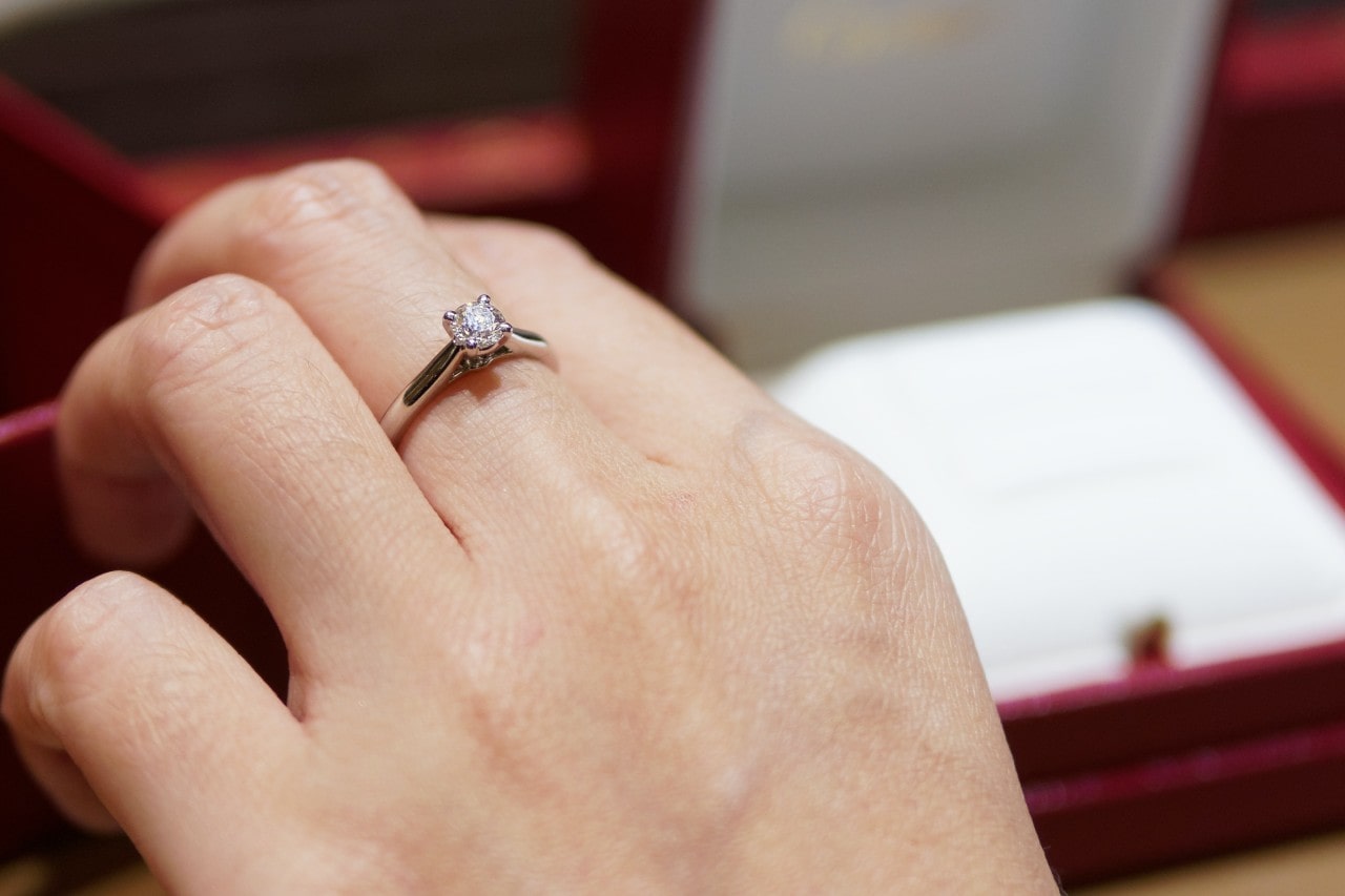 A close-up of a hand wearing a silver engagement ring with a single round diamond set in a prong setting.