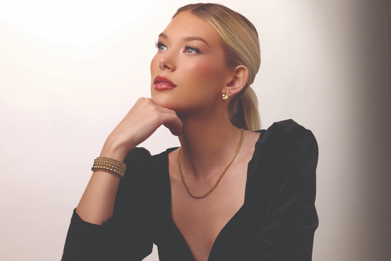 A woman wearing a bold statement necklace and ring with her hand on her upper chest.