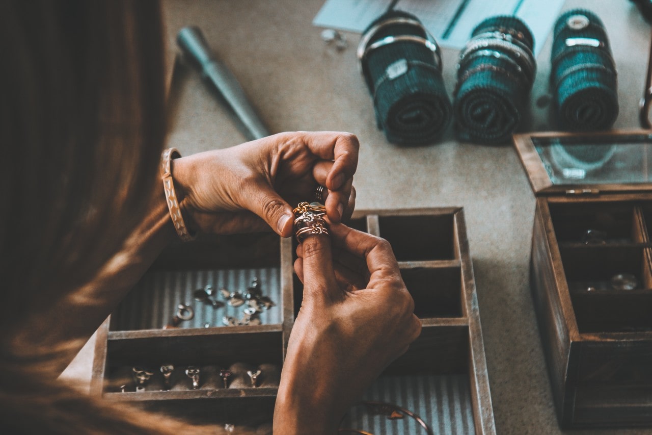 An expert examining some braided golden rings from a jewelry box with other jewelry strewn about.