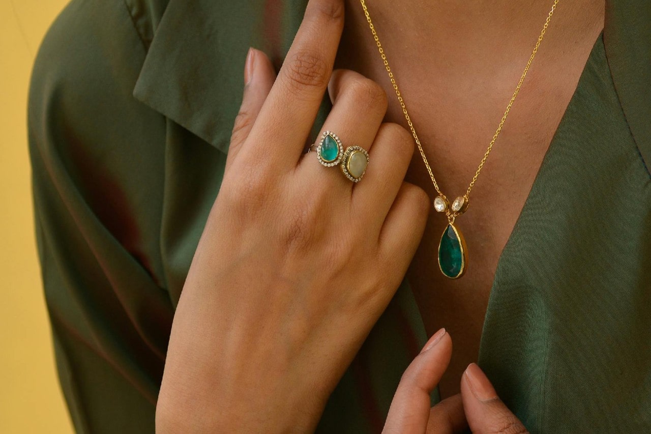 Woman in green shirt wearing a teardrop green pendant and matching green gemstone rings.