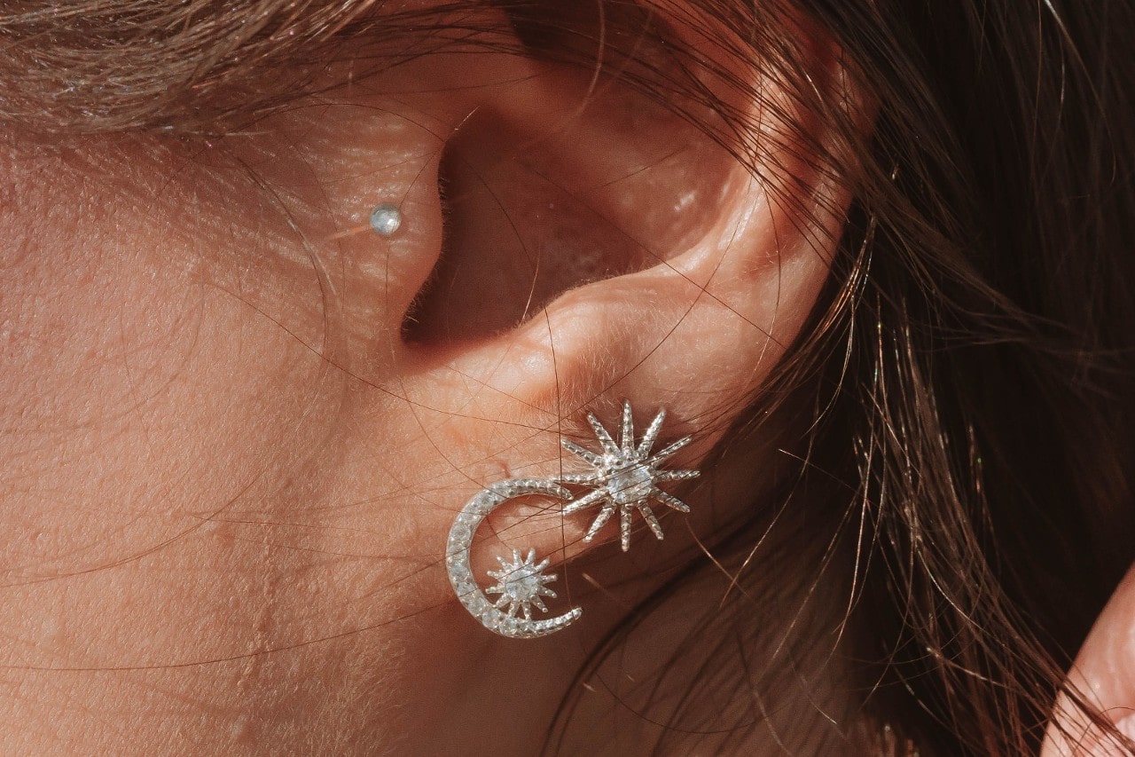Close‑up of an ear wearing a pearl and a diamond‑set moon‑sun earring.