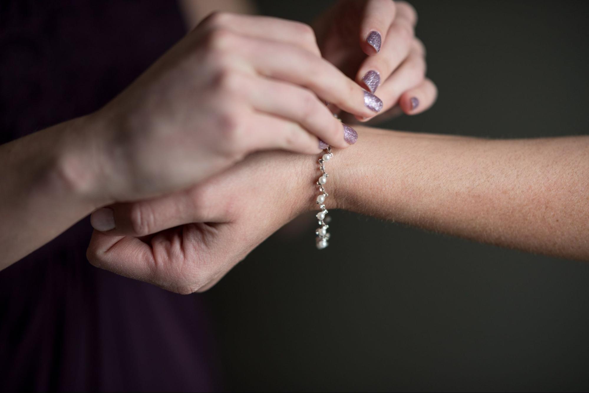 Close up of hands fastening a delicate pearl bracelet against a dark background.