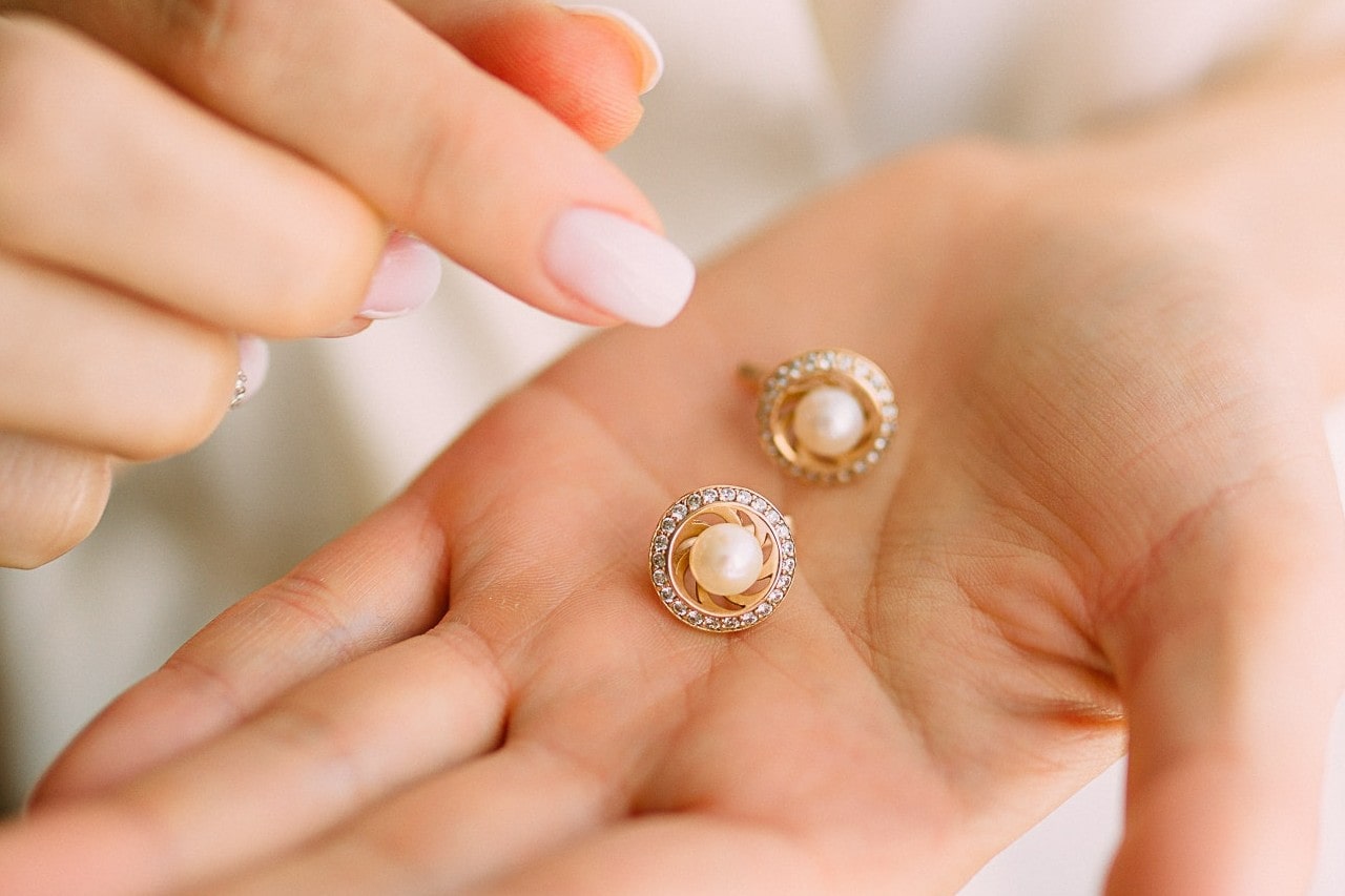 A pair of elegant pearl earrings with gold and diamond accents rest in an open palm.