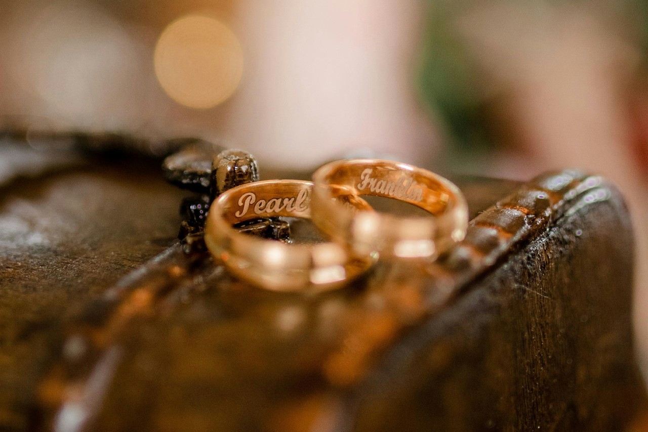 Two yellow gold wedding bands with engraved names lay on a rustic wooden surface.
