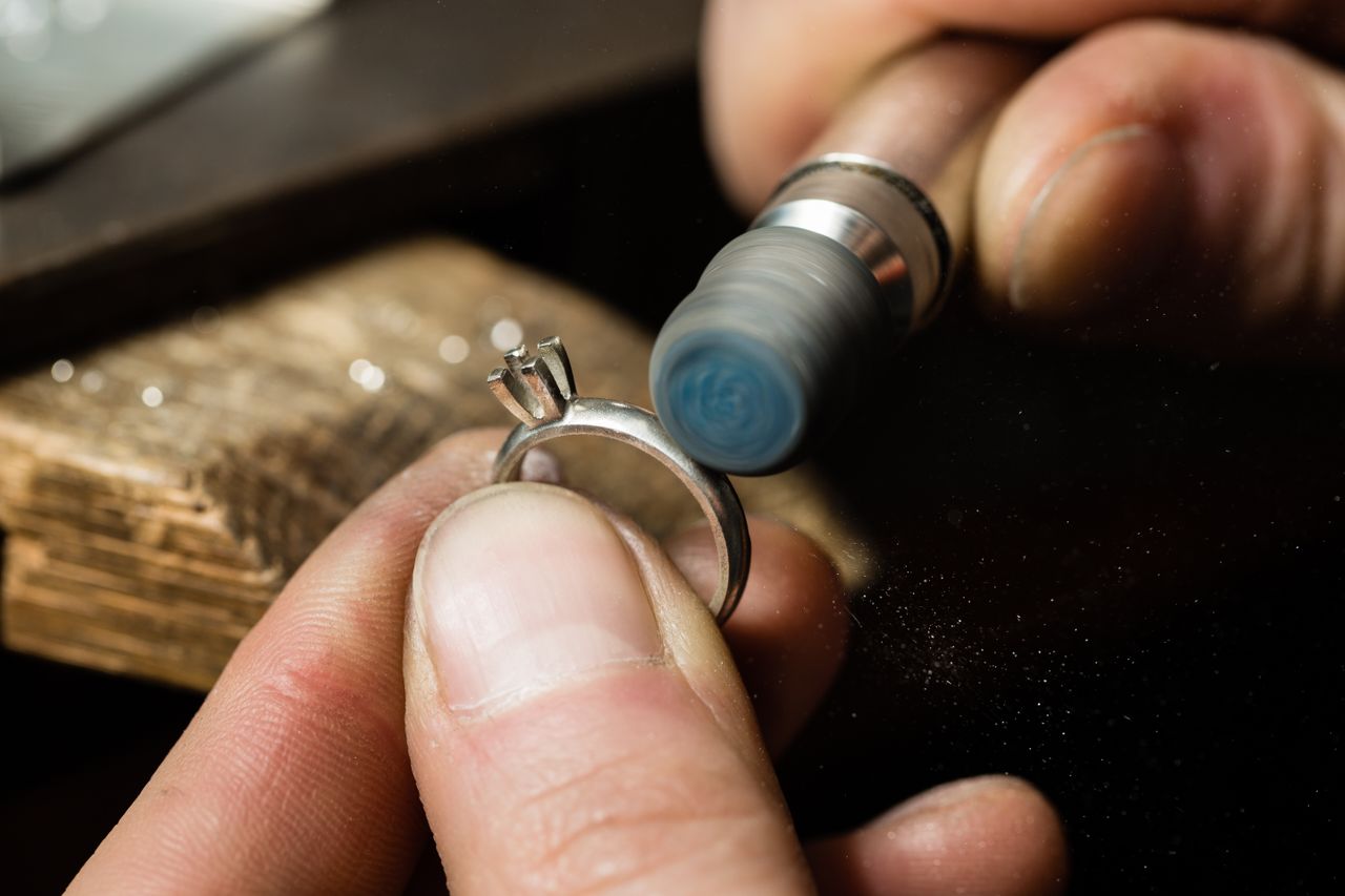 A close up of a jeweler polishing a solitaire ring without a stone.