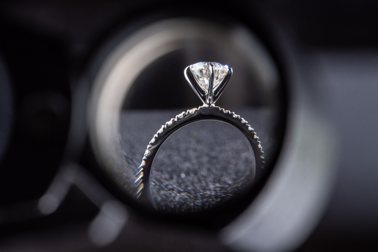 A shot of a diamond engagement ring on a black textured surface from a matching wedding band.
