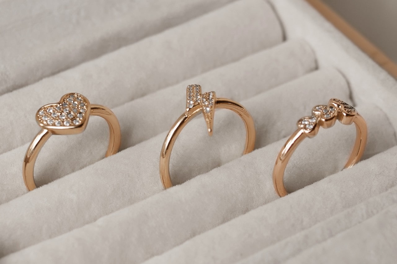Three gold rings with sparkling designs are displayed in a white jewelry box.