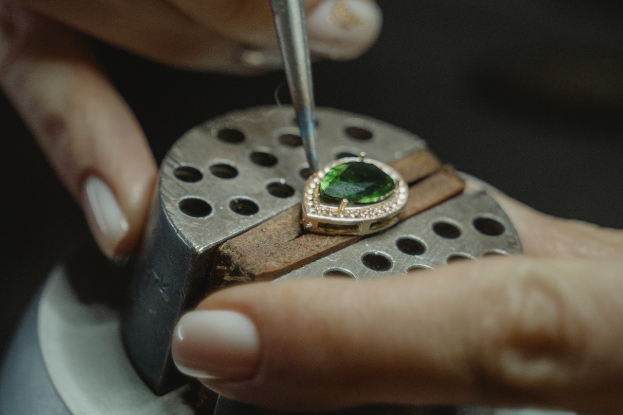 A close up of a jeweler working on a pear shaped halo emerald pendant.