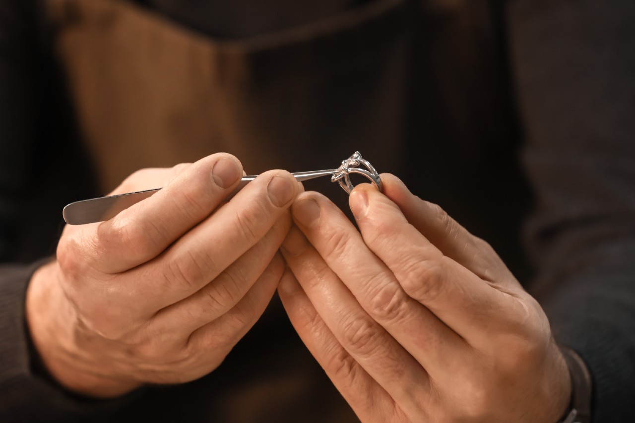 A close up of a jeweler with tweezers fixing stoned on a split-shank white gold ring.
