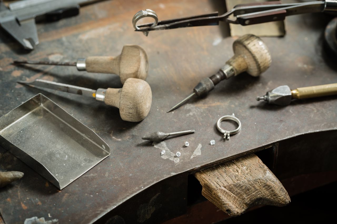 Jewelry-making tools and loose diamonds are arranged on a craftsman’s workbench with an unfinished ring.