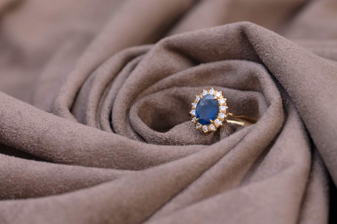 A rose gold halo ring with a sapphire center stone, delicately nestled within the folds of soft, brown fabric.
