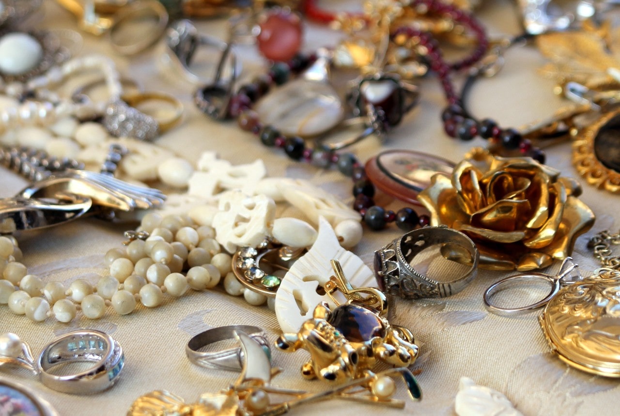 A bunch of different metals and jewelry styles laid out on a table cloth, including rings, gold, pearls, and broaches.
