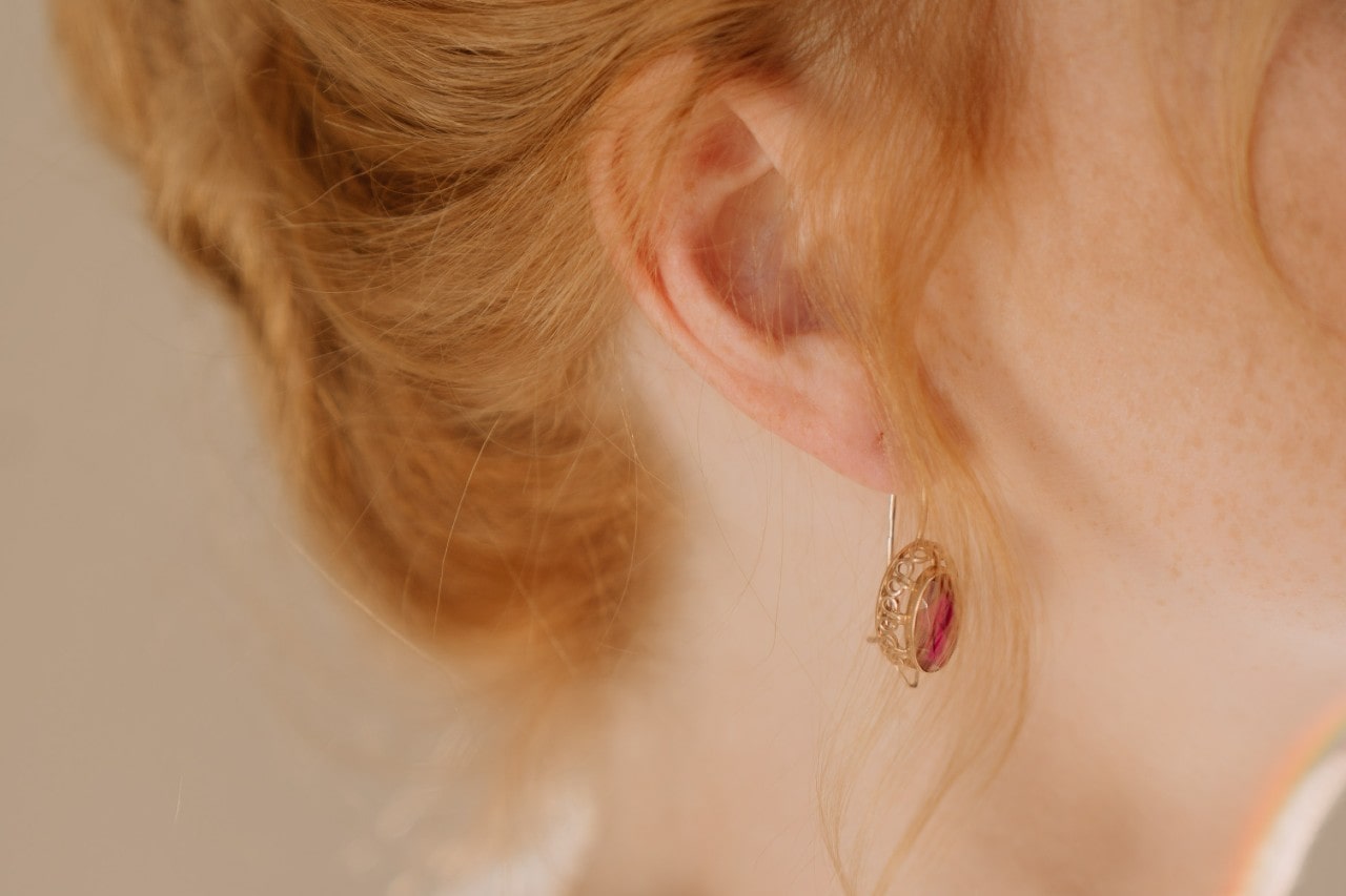 A close-up of a woman with ginger hair wearing a yellow gold vintage earring with an oval ruby.