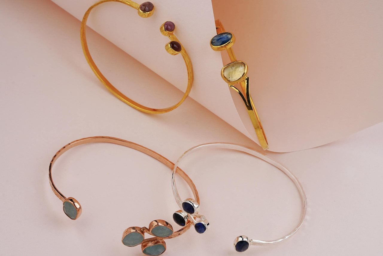 Several bracelets in yellow, rose and white gold with gemstones on a beige surface.